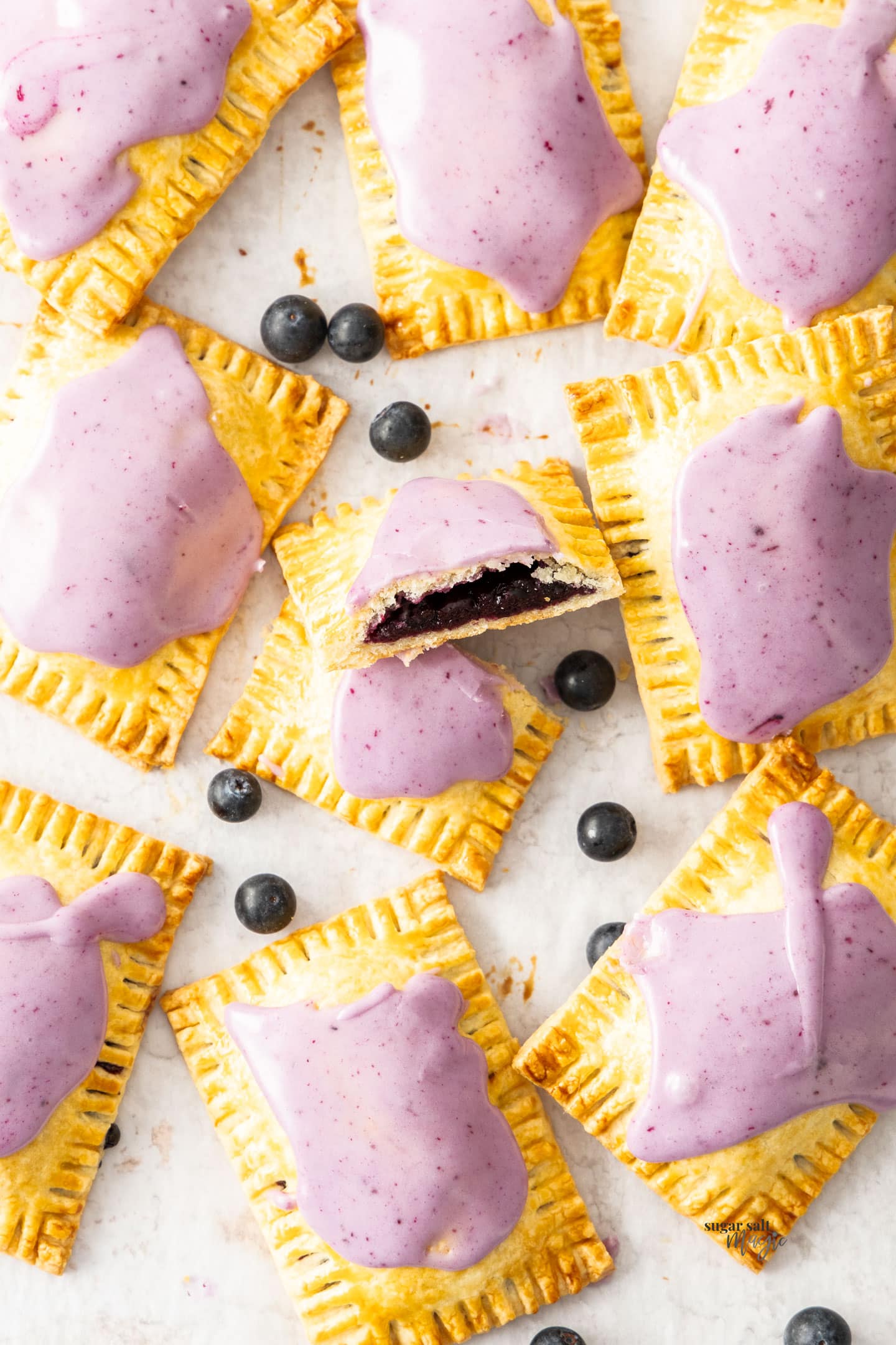 Top down view of a batch of 9 blueberry pop tarts with one cut in half.