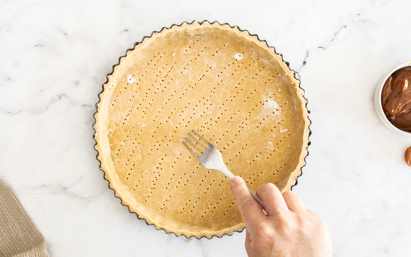 A hand using a fork to dock the tart shell base.