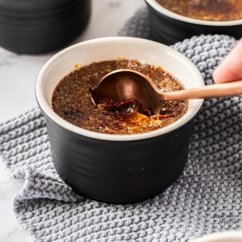 A spoon cracking the sugar top of a creme brulee.