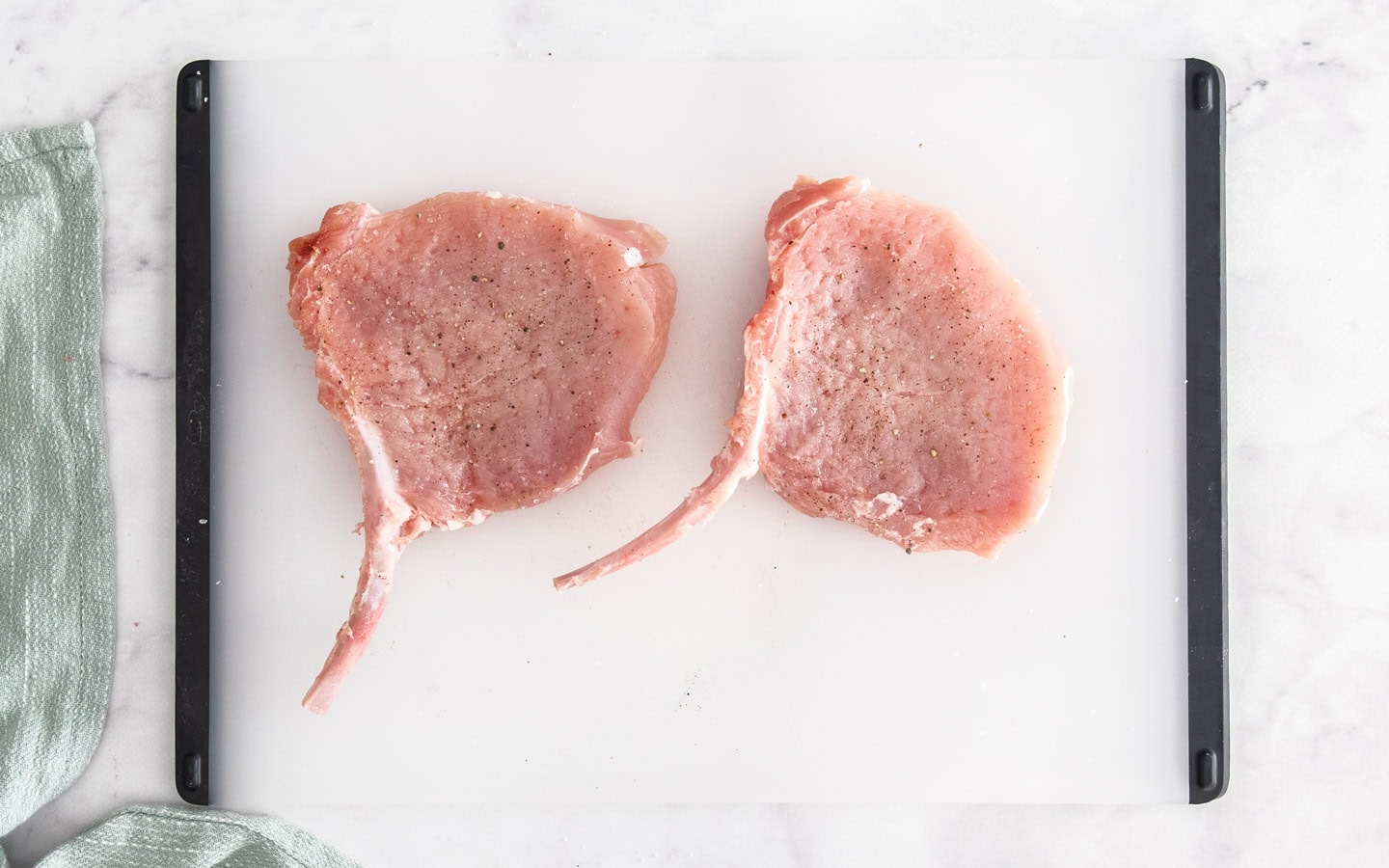 Two raw pork cutlets on a chopping board.
