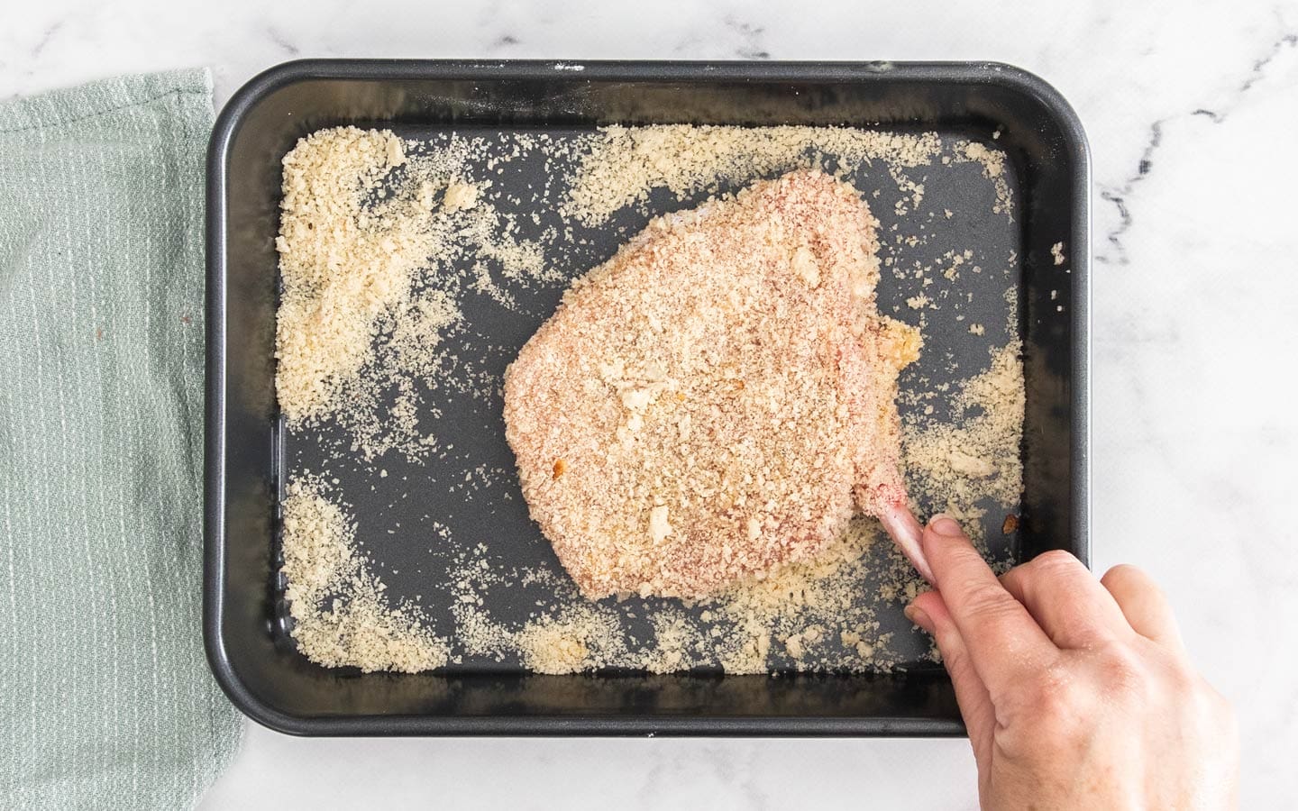 A pork cutlet being coated in bread crumbs.