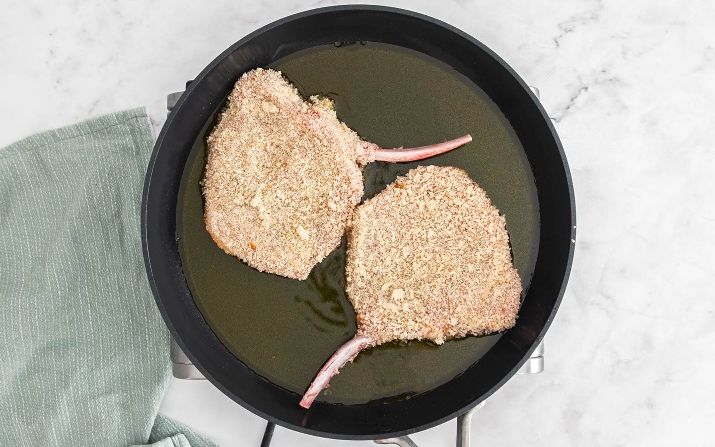 Two pork cutlets in a frying pan beginning to fry.