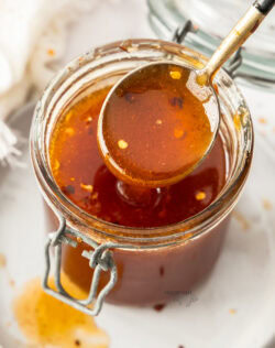 A spoon taking some hot honey out of a jar.