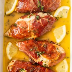 Top down view of 4 baked chicken breasts in a casserole dish with lemon slices.