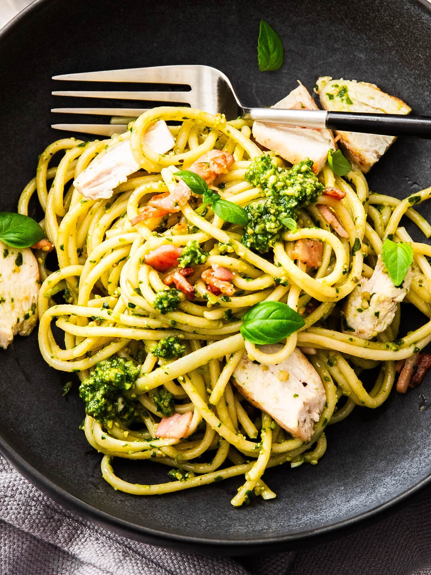 Super close up top down view of a black bowl with a serve of chicken pesto pasta.