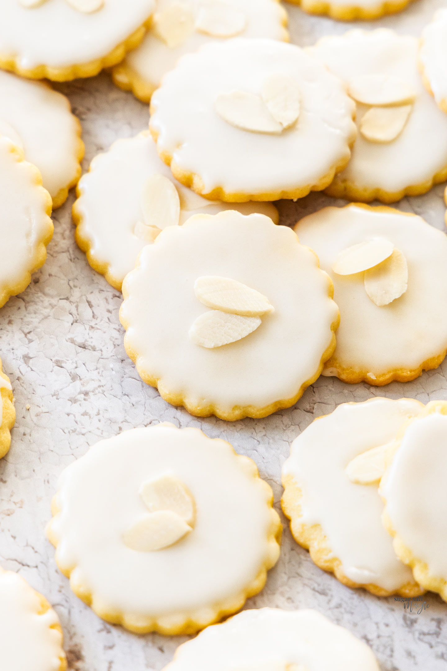 A pile of almond cookies topped with icing and flaked almonds.