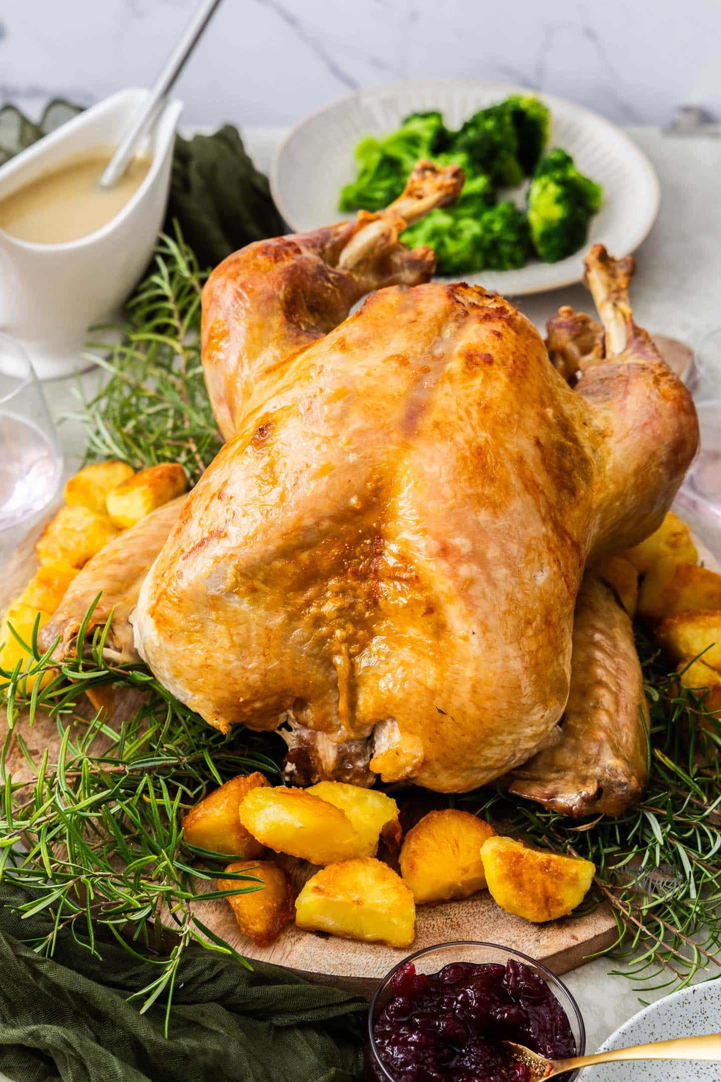 A whole roasted turkey on a wooden board with rosemary and potatoes.