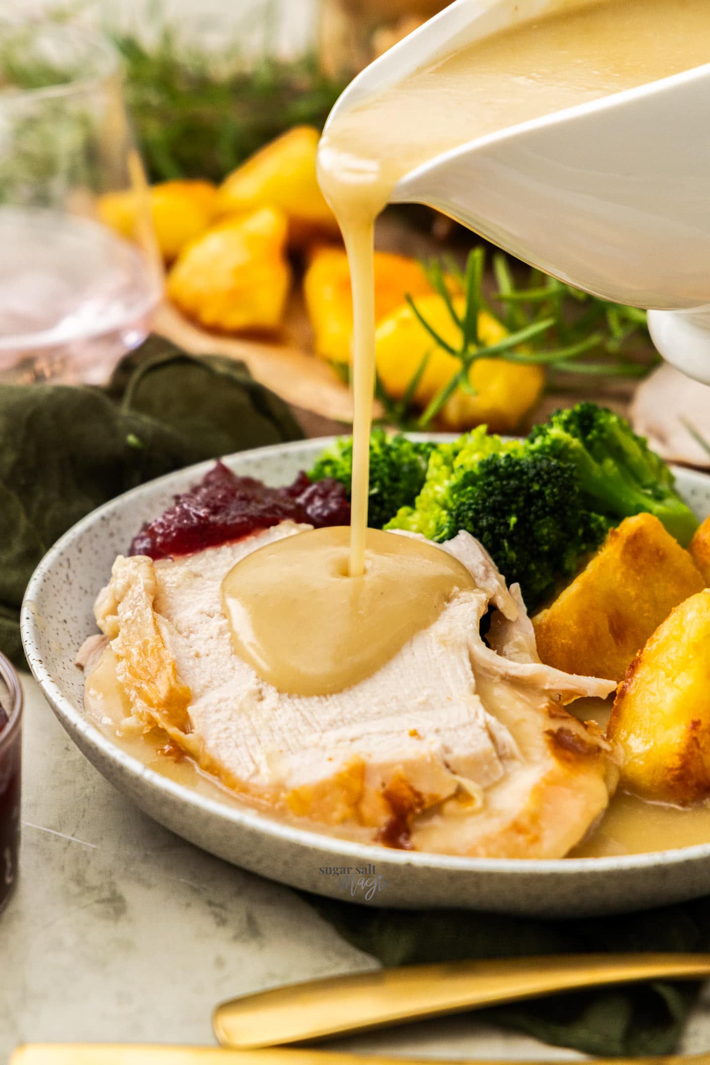 Gravy being poured from a gravy boat onto slices of turkey on a plate.