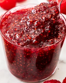 Looking into a glass of raspberry jam with a spoon digging in.