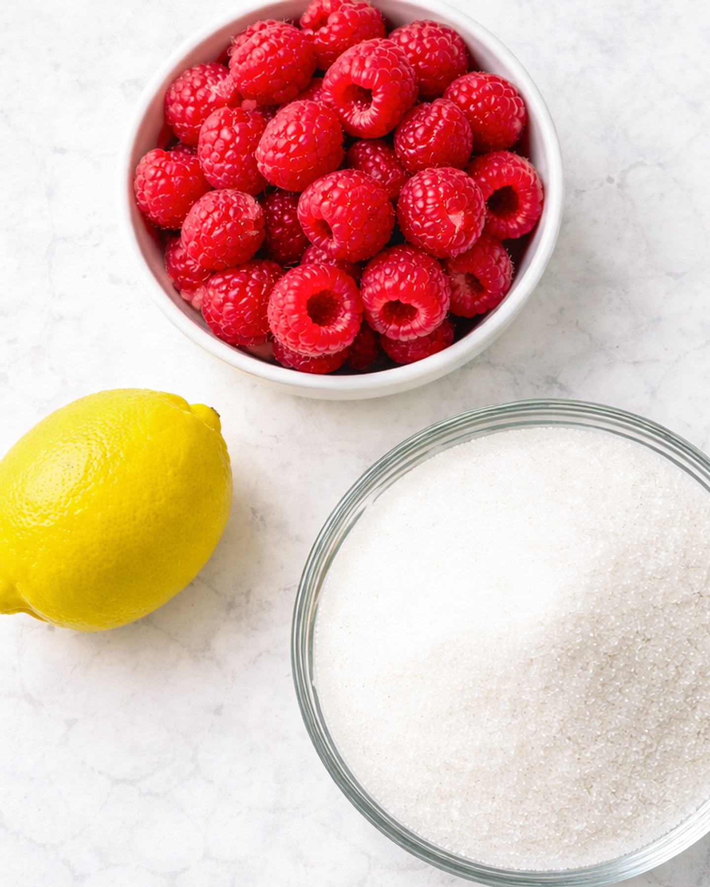Easy Raspberry Jam Ingredients for homemade raspberry jam on a marble surface.