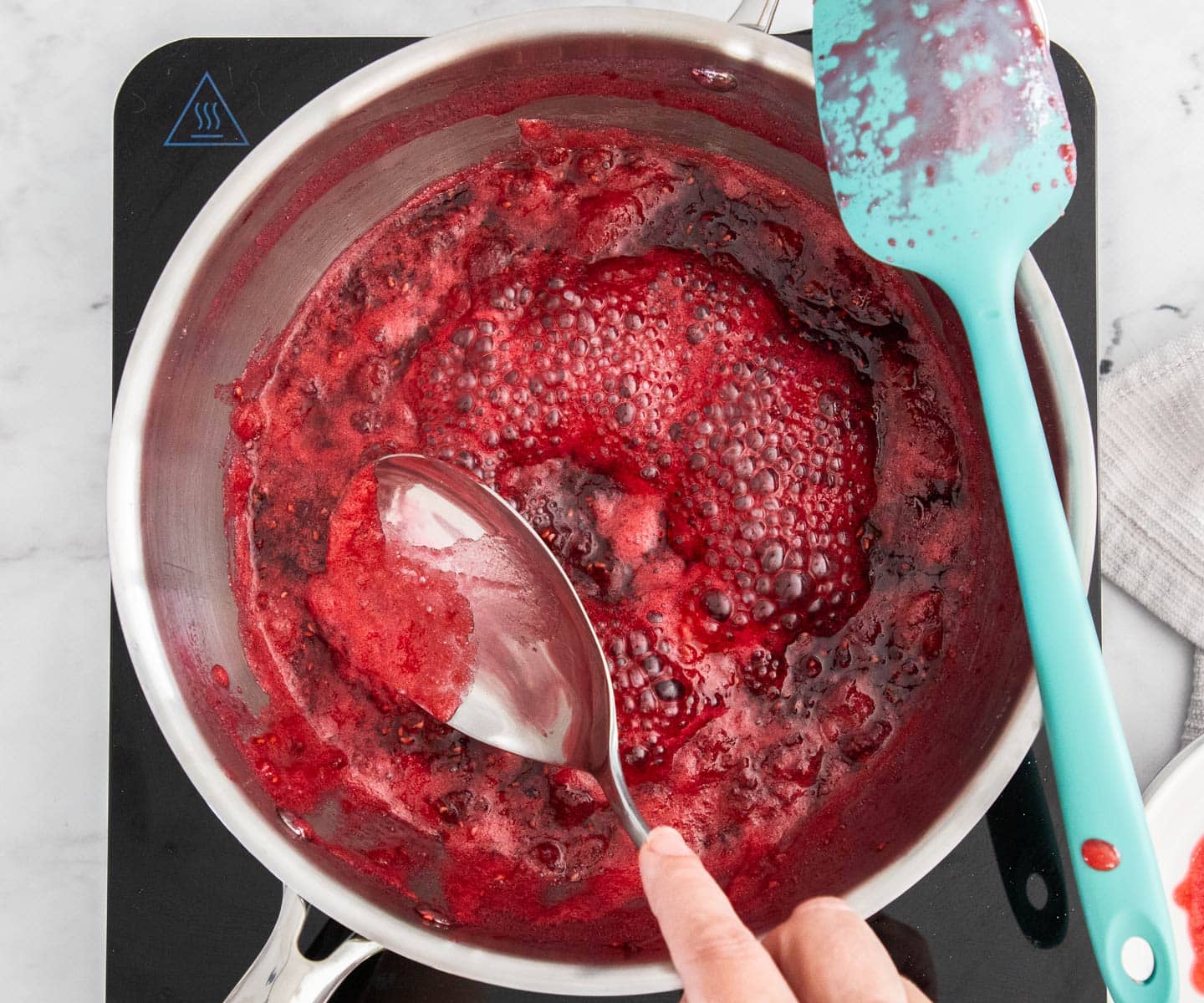 Easy Raspberry Jam Scooping the residue off the jam in a saucepan.