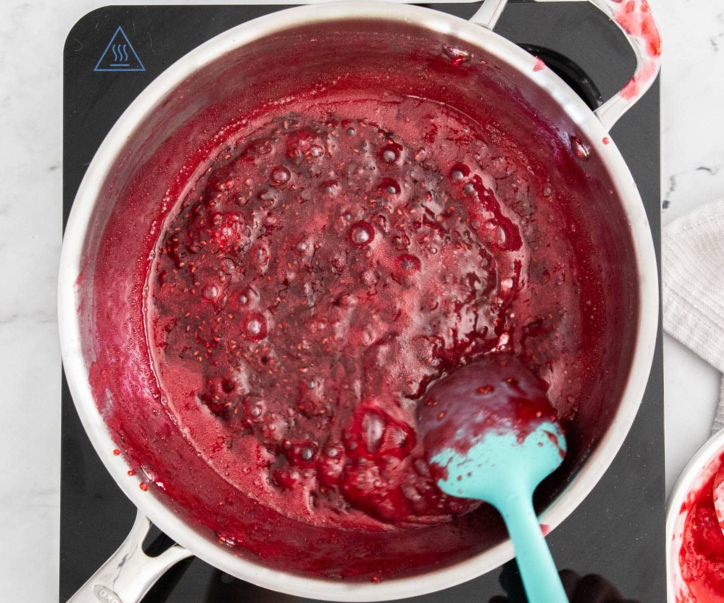 Easy Raspberry Jam The jam getting very thick and being stirred in a pan.