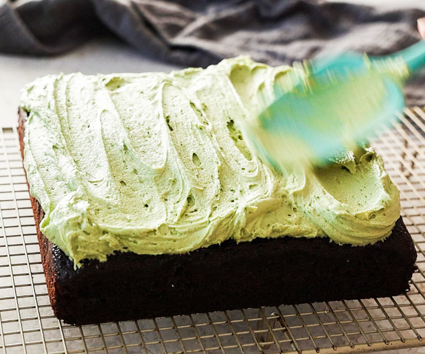 Pistachio Chocolate Snack Cake A spatula spread the buttercream over the cake.