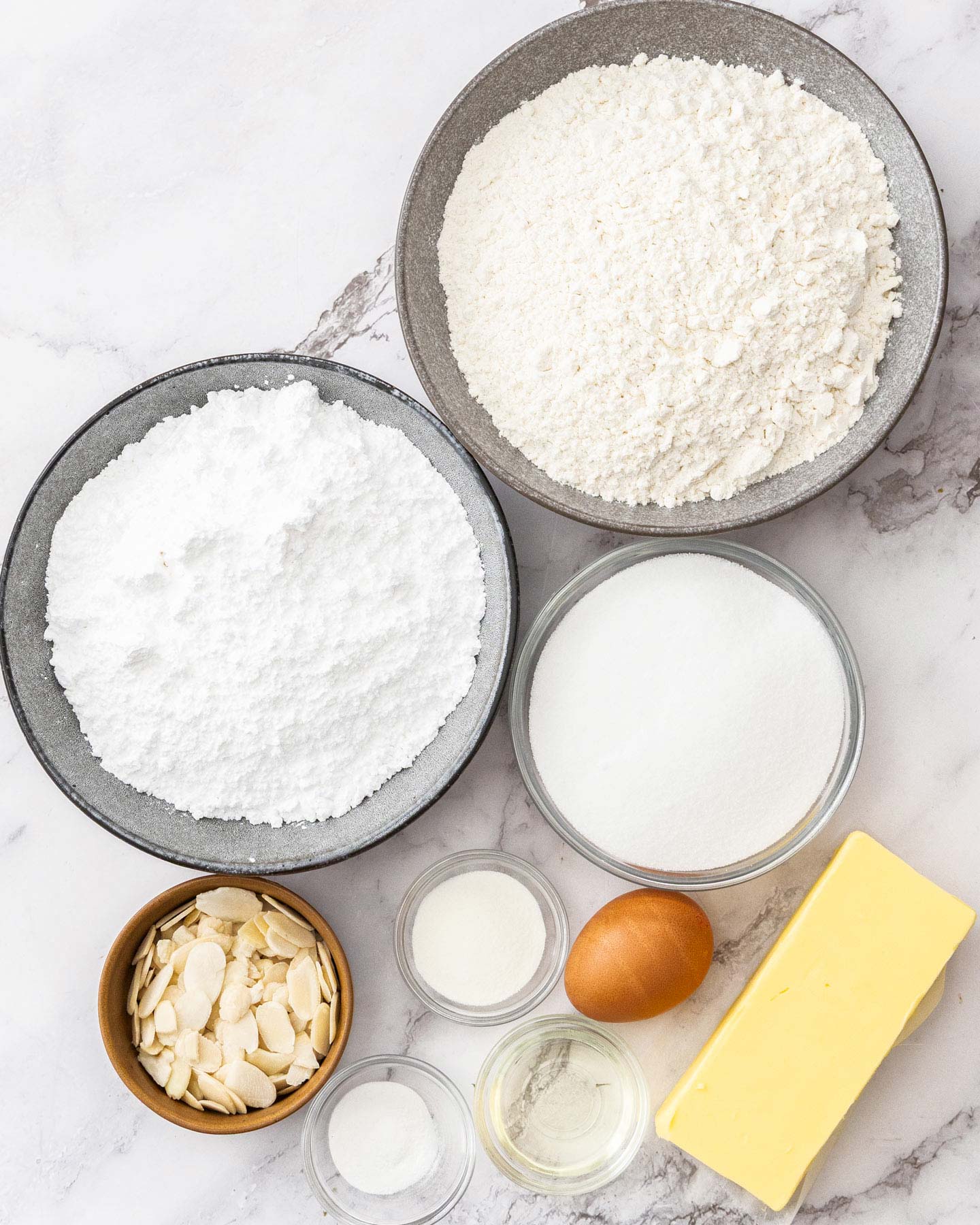 Top down view of ingredients for almond sugar cookies on a marble surface.