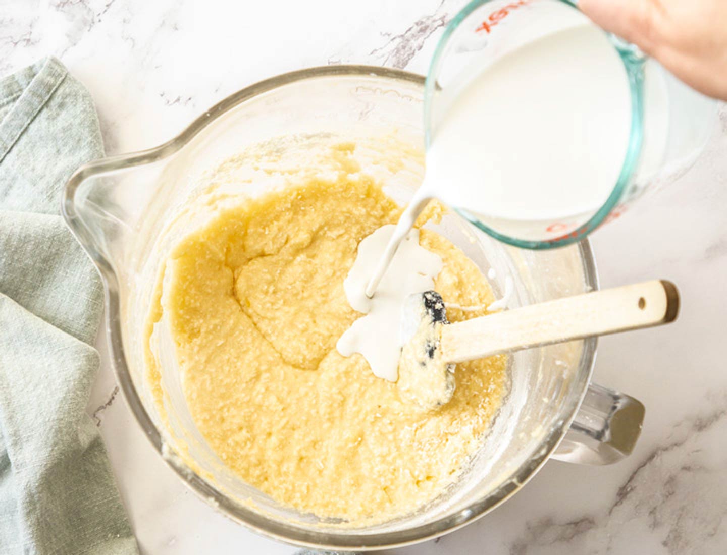 Raspberry Coconut Cake Pouring coconut milk into the batter in a glass mixing bowl.