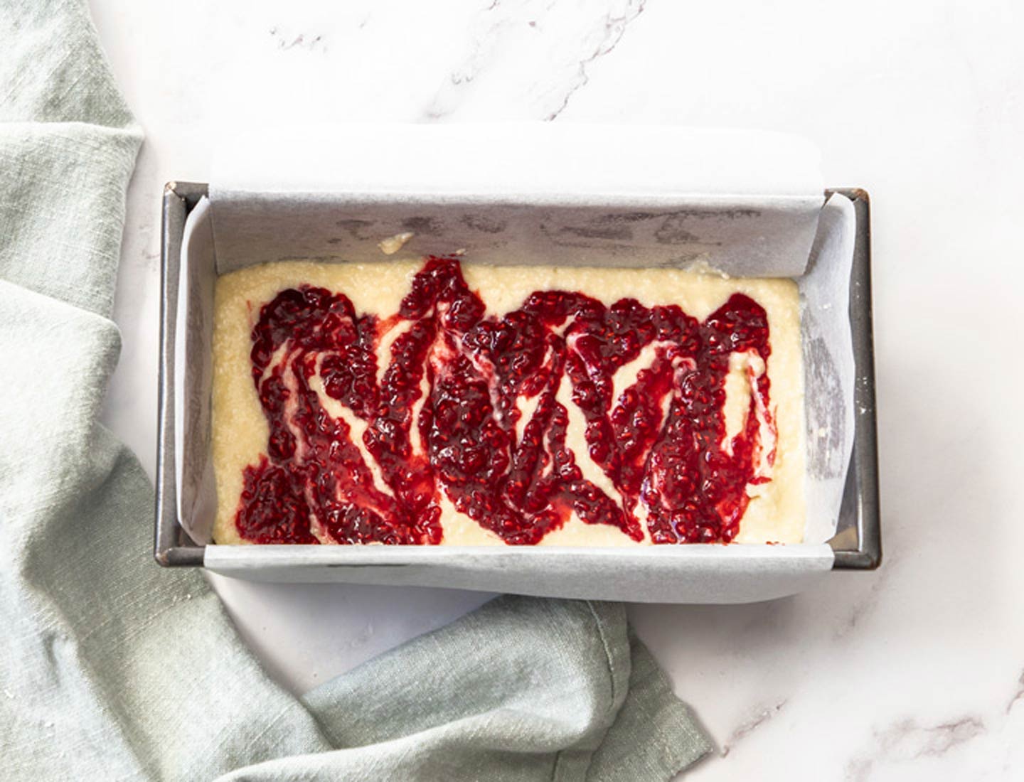 Raspberry Coconut Cake Raspberry compote swirled over the cake batter in a baking pan.