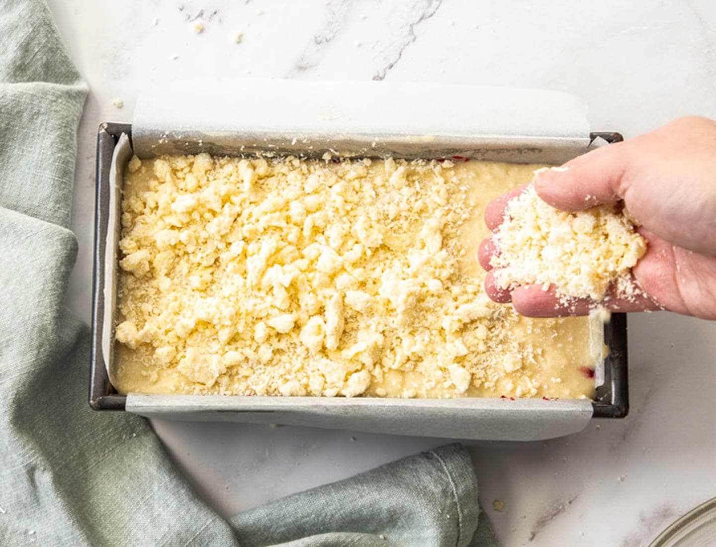 Raspberry Coconut Cake A hand scattering crumble over the top of the cake batter in the baking pan.