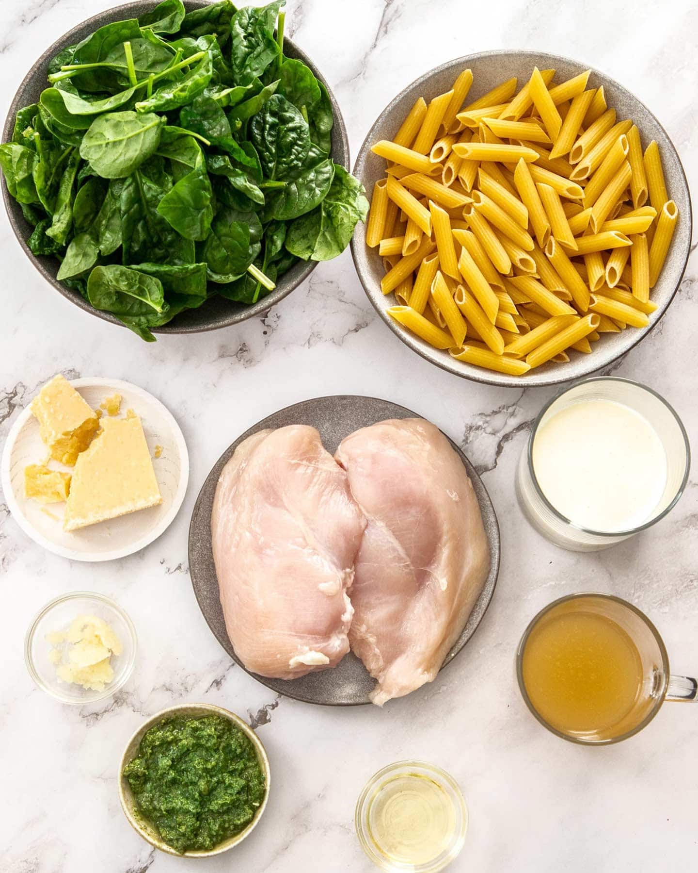 Creamy Chicken Spinach Pasta Ingredients for creamy chicken spinach pasta on a marble surface.